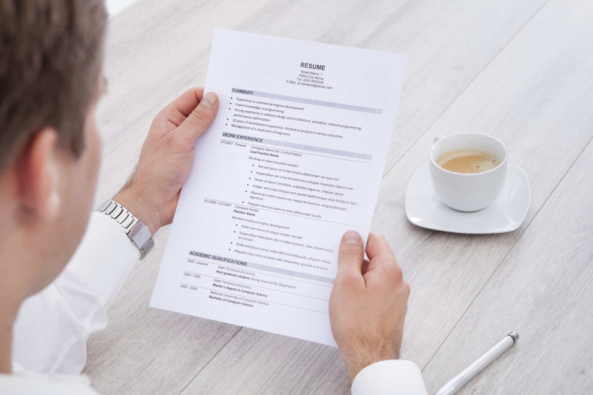 Businessman Reading Resume With Tea Cup On Desk